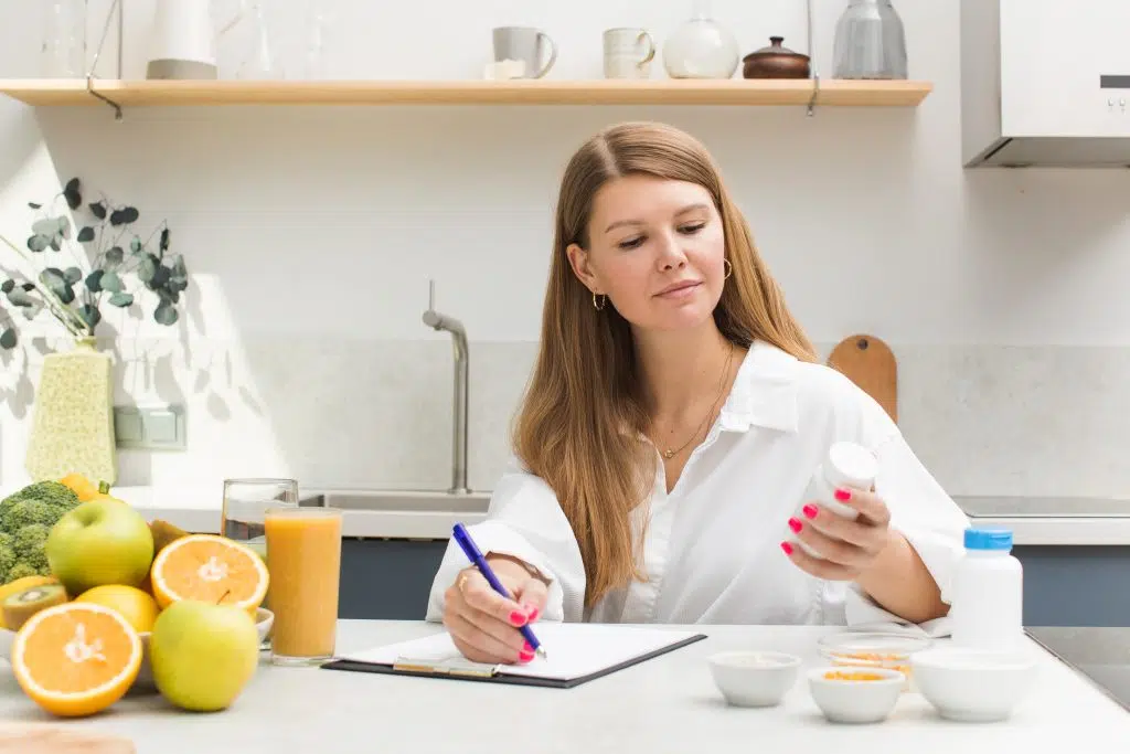 A nutritionist writes an appointment for taking food supplements and vitamins at a table with fresh fruits and vegetables. The concept of a healthy lifestyle.