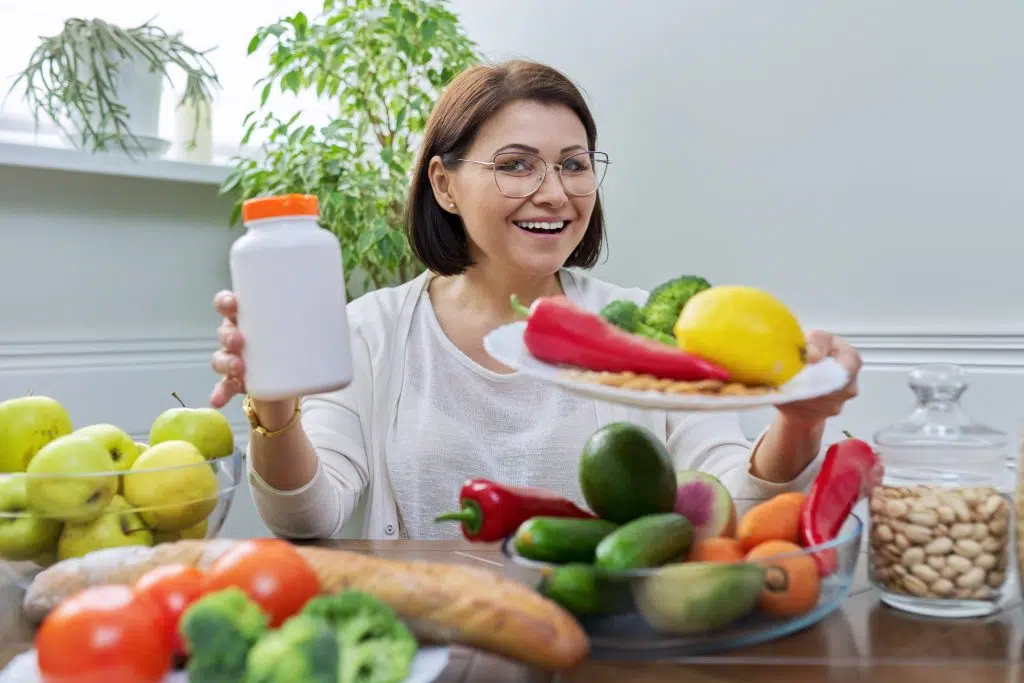 Woman nutritionist with plate set of healthy food and jar of food supplement. Female looking at camera, on table vegetables fruits bread cereals nuts. Natural organic eco products, diet, vegetarianism